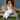 Linen White Florence Pant placed on a model sitting on the front porch of a blue and wood building