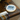 A small wooden embroidery hoop holding white fabric with a blue stitched design and the words “YES WE CAN,” placed on a dark wooden table. A needle is threaded, and a card showing thread color options hangs below.