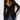 A woman modeling a black sheer lace long-sleeve top with ruffle trim over a dark undergarment, paired with blue jeans and a black belt, against a plain white studio background.