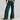 A model wearing a dark green ribbed knit crop top and matching dark green wide-leg pants, standing against a light gray studio background.