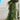 A lush green evergreen garland draped over a white wooden crate on a rustic wooden table, set against a white brick wall. A blue 'NEW!' banner is in the top-left corner.