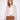 A woman modeling a light beige open-front cardigan with multicolored flecks, worn over a white top and brown corduroy pants, against a plain white studio background.