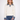 A woman modeling a cream-colored knit sweater with a contrasting blue denim collar and matching denim cuffs, paired with blue jeans, against a plain white studio background.