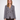 A woman modeling a double-breasted houndstooth blazer in black, white, and blue, paired with dark brown trousers, against a plain light gray background.