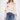 A woman modeling a cream-colored chunky knit sweater with colorful embroidered flowers, paired with blue jeans, against a plain white studio background.