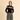 A woman modeling a black long-sleeve knit sweater with a textured beige geometric pattern across the chest, paired with high-waisted gray wide-leg trousers, against a solid beige studio background.