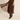 A woman models a dark brown ribbed short-sleeve knit top paired with a matching brown pleated tulle midi skirt and dark brown heeled ankle boots, set against a plain beige studio background.