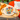 A close-up of a circular embroidery hoop containing a floral needlepoint or cross-stitch design in bright colors, placed on a wooden table. Orange yarn is draped nearby, and part of another hoop with a floral outline is visible in the background on an orange chair.